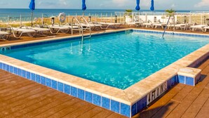 Ein Swimmingpool mit blauen Fliesen, Liegestühlen und Sonnenschirmen auf einer Holzterrasse.