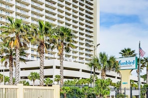 A high-rise building with a sign for 'Sunbird Condominiums' and a gated entrance. - Designer beachfront Gulf-view condo - beach access, pools, tennis, shuffleboard (Panama City Beach)