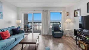 Una sala de estar con sofá, sillón, mesa de centro, televisor y un balcón con vistas.