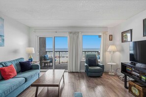 A living room with a sofa, armchair, coffee table, TV, and a balcony with a view. - 3rd-floor open, airy condo with great views - close to dining (Fort Walton Beach)