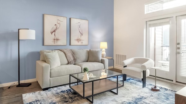 A modern living room with a sofa, a coffee table, a floor lamp, and two wall-mounted paintings. - Landing | Spectacular 1BD, Pool, Gym (Colorado Springs)