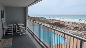Een balkon met uitzicht op het strand, een zwembad en een tafel met stoelen.