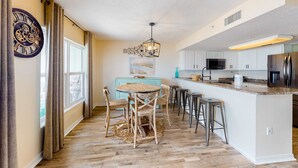 Een moderne keuken met een centraal eiland, barkrukken en een eettafel met stoelen.