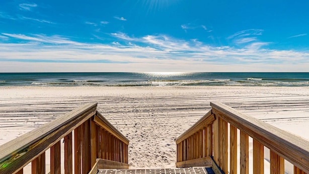 Een houten strandboulevard die leidt naar een zandstrand met golven.