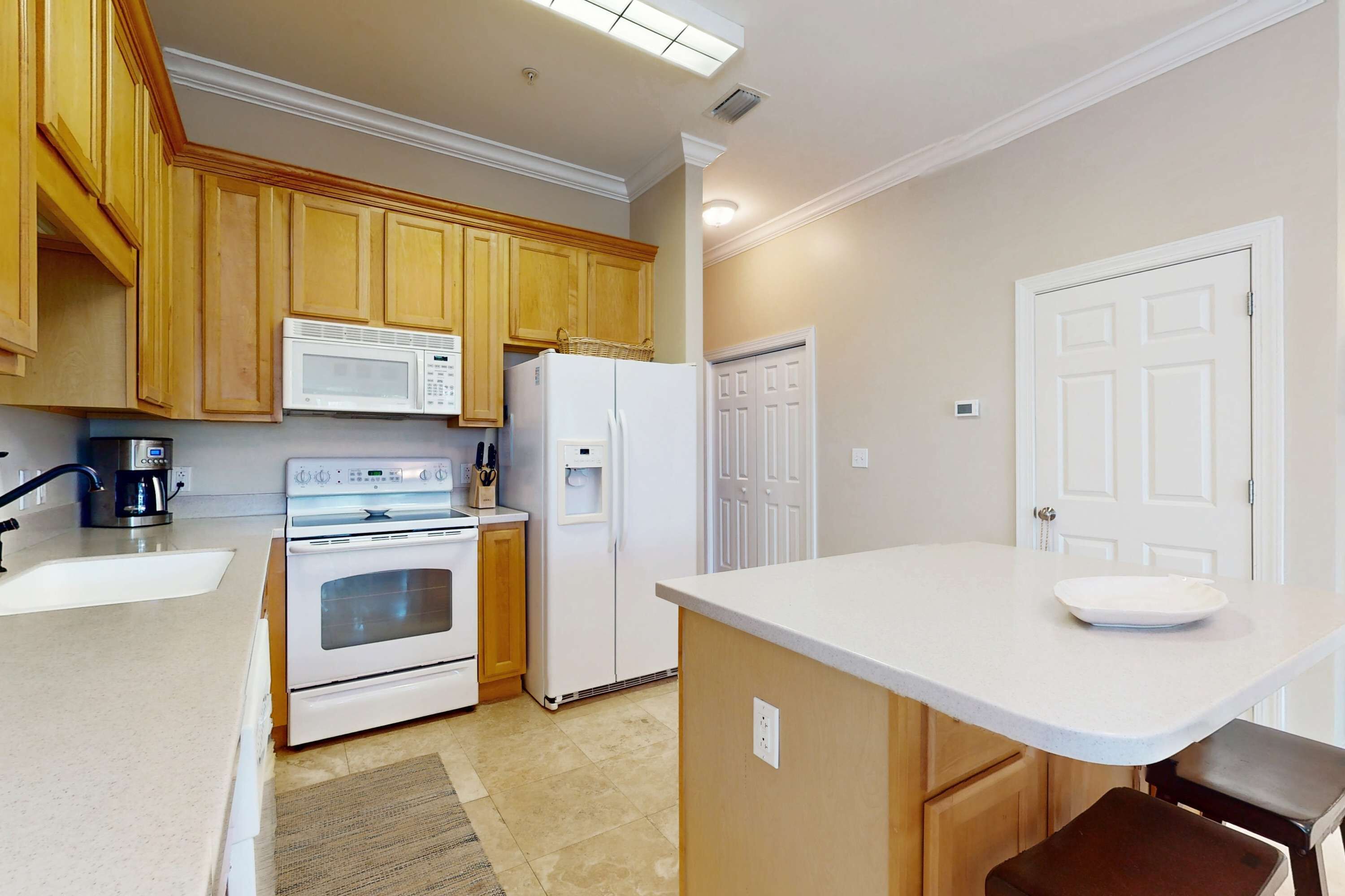 A kitchen with wooden cabinets, a white microwave, a refrigerator, an oven, a sink, and a small island with a bowl.