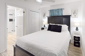 Ein Schlafzimmer mit Bett, Nachttischen, Deckenventilator und einer Tür zu einem Badezimmer.
