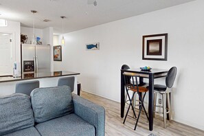 Ein modernes Wohnzimmer mit einer Couch, einem Esstisch mit Stühlen, einer Küchenzeile mit Kühlschrank und einem Bilderrahmen an der Wand.