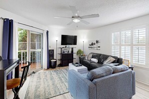Ein Wohnzimmer mit einer Couch, einem Fernseher, einem Deckenventilator und einer Schiebetür zu einer Terrasse.