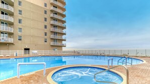 A swimming pool area with a hot tub, surrounded by a brick patio, and adjacent to a high-rise building with balconies. - Spacious Gulf front condo w/shared hot tub, pools, gym - close to dining (Panama City Beach)