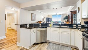 A spacious kitchen with white cabinets, a black countertop, and a dishwasher. - Spacious Gulf front condo w/shared hot tub, pools, gym - close to dining (Panama City Beach)