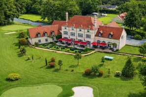 A large building with multiple red-roofed structures, a well-maintained lawn, and a golf course. - Logis Hôtel Domaine de l'Orangerie (Bonnat)