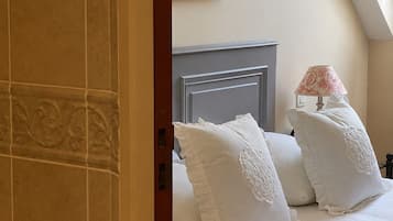 A bedroom with a bed, pillows, a nightstand, a lamp, and a window with curtains.
