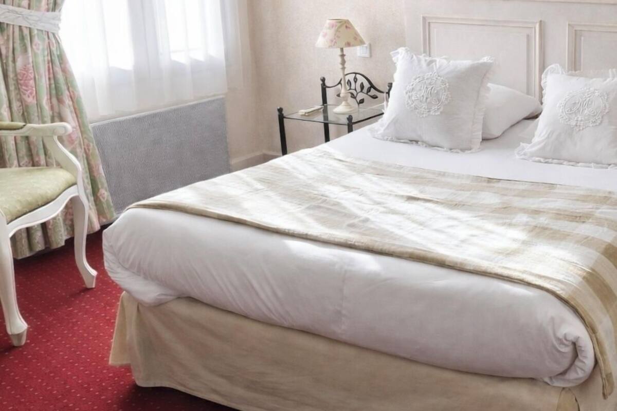A hotel room with a bed, a chair, a lamp, and a mirror.