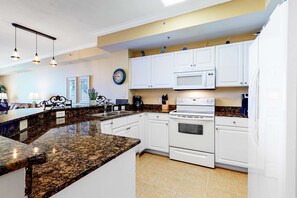 A kitchen with white cabinets, a granite countertop, a microwave, an oven, and a clock on the wall. - 15th Floor Oceanfront Condo with Shared Pool & Hot Tub, Ocean View, & Fast WiFi (Panama City Beach)