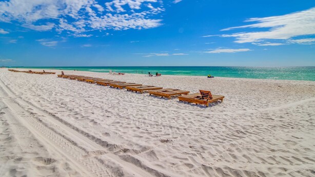 Ein Strand mit in Reihn gestelltem Holzliegestühlen.