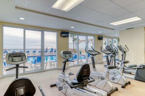 A gym with cardio machines and a view of a pool and lounge chairs. - Oceanfront condo with pool, hot tub, splash pad & gym - great location (Panama City Beach)