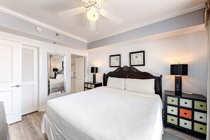 Une chambre à coucher avec un lit, une commode, un miroir et un ventilateur de plafond.