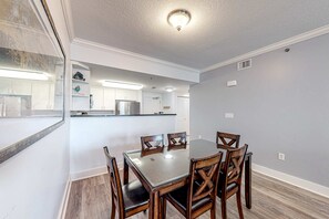 Un coin repas avec une table à plateau en verre, des chaises en bois et une cuisine en arrière-plan.