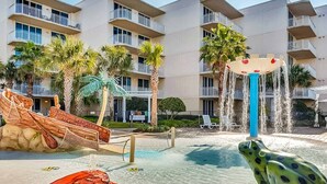 A hotel pool area with a water slide, a frog statue, and a palm tree. - Welcoming, Coastal Condo On Okaloosa Island Playground, 2 Hot Tubs (Fort Walton Beach)