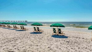 A beach with rows of green umbrellas and lounge chairs. - Welcoming, Coastal Condo On Okaloosa Island Playground, 2 Hot Tubs (Fort Walton Beach)