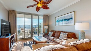 En rummelig stue med stor sofa, sofabord og fjernsyn. Der er en balkon med udsigt over byen.