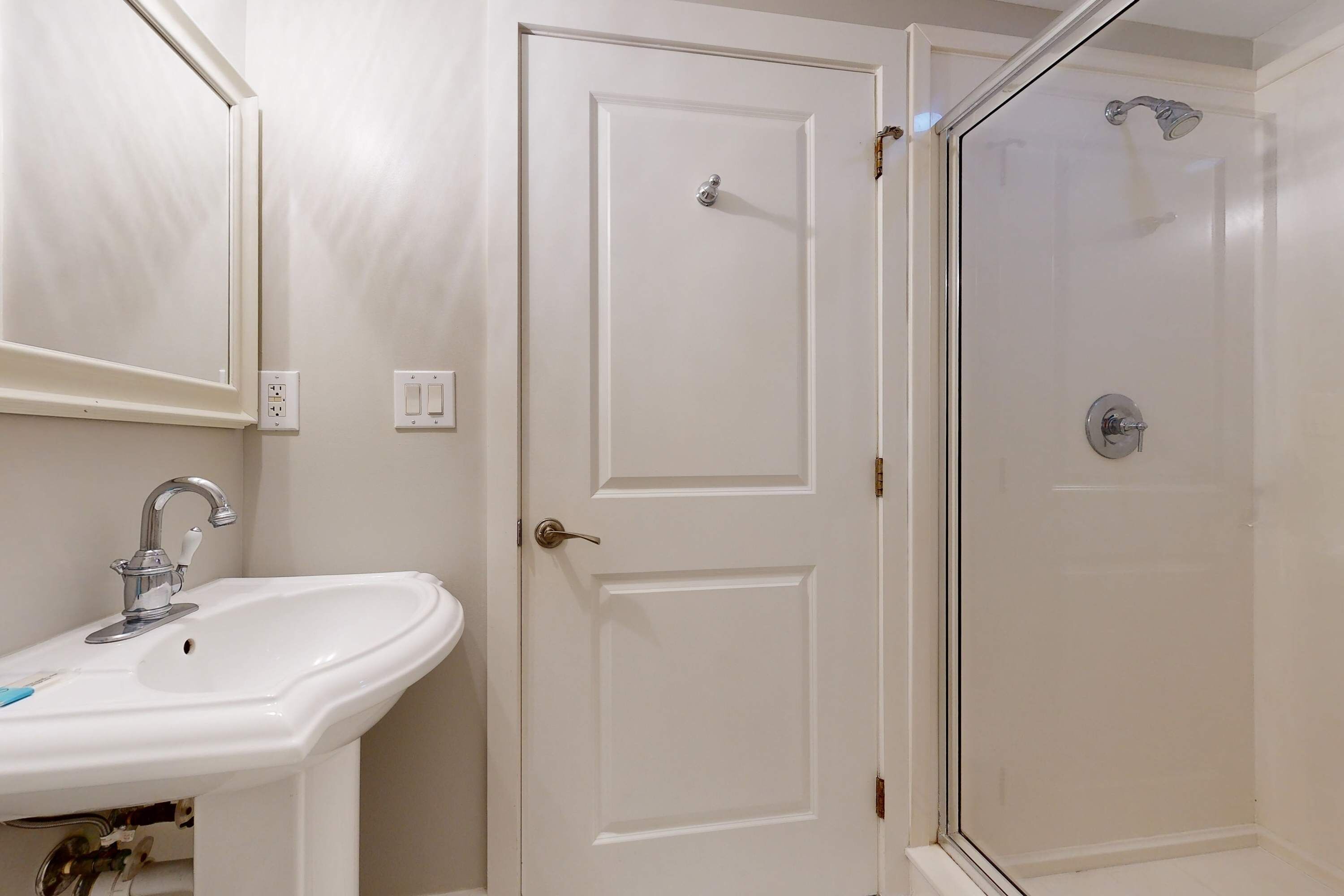 A bathroom with a white sink, a door, and a shower enclosure.