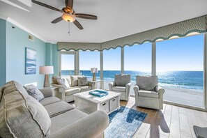A spacious living room with a view of the ocean, featuring a ceiling fan, a large window, and a light-colored sofa set. - Picture-Perfect Beach-Front Condo At Waterscape 490 Feet Of Private Beach (Fort Walton Beach)