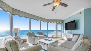 A spacious living room with a view of the ocean, a ceiling fan, and a flat-screen TV.