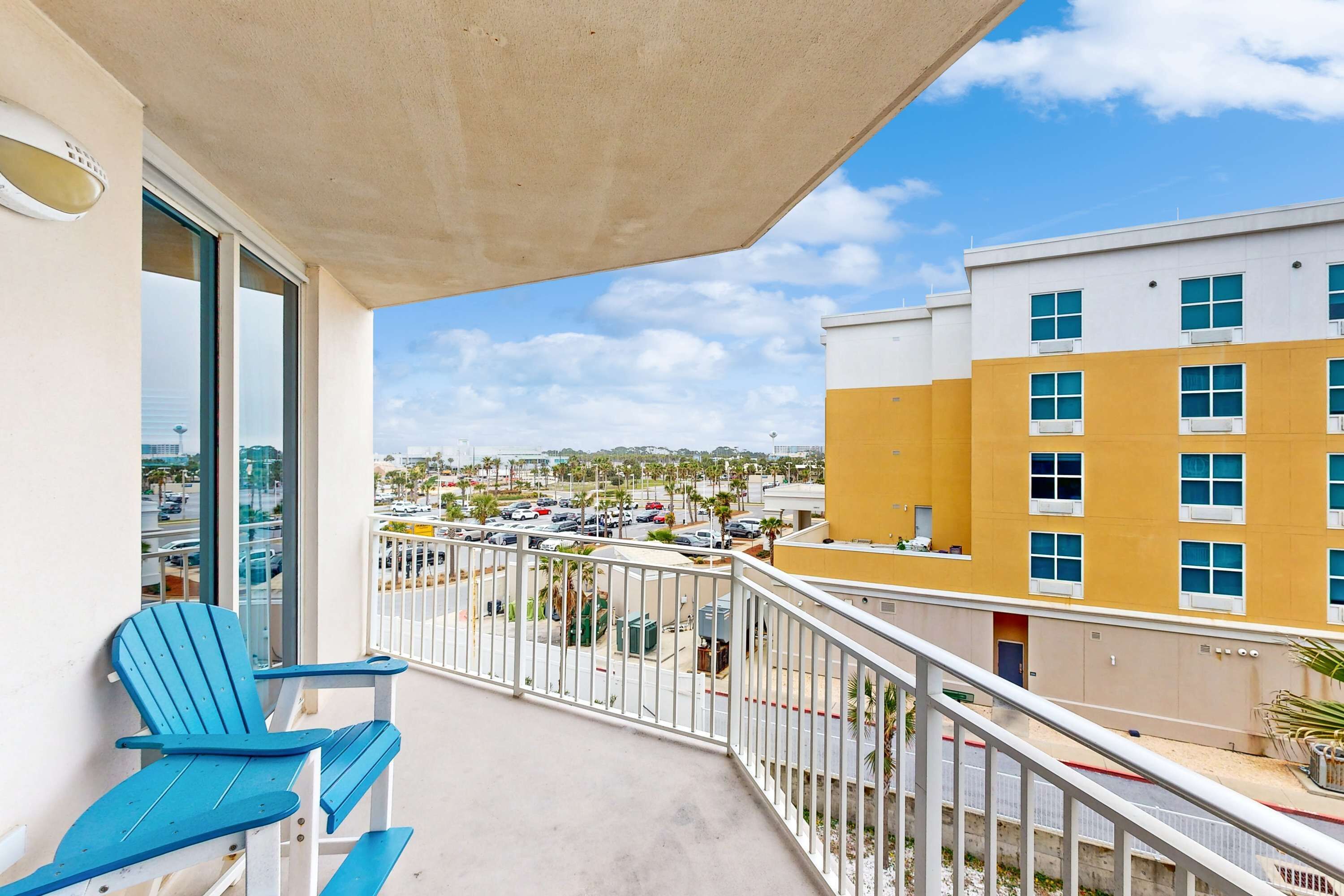 Un balcon avec deux fauteuils Adirondack bleus, un sol en béton et une vue sur un parking et des bâtiments en arrière-plan.