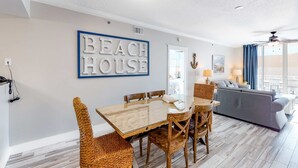 Una sala moderna con un sofá grande, una mesa de comedor con sillas y un letrero en la pared que dice "BEACH HOUSE".