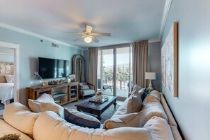 Ein Wohnzimmer mit großem Flachbildfernseher, Deckenventilator, einer Couch und einem Couchtisch.