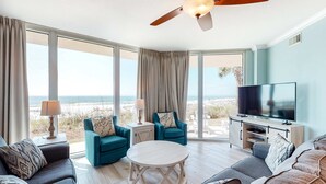 A spacious living room with a large TV, comfortable seating, a ceiling fan, and a view of the beach. - Exquisite, Gulf-front, 1st-floor condo At Waterscape Waterfall, lazy river (Fort Walton Beach)
