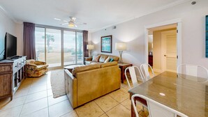 A living room with a sofa, a dining table, and a TV. - Sunny Waterscape ground-floor condo with pools, hot tubs, & stunning Gulf views (Fort Walton Beach)