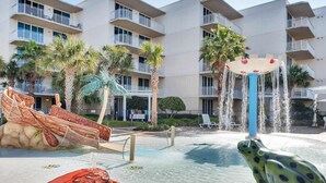 A pool area with a water slide, a frog statue, and a netted play area. - Sunny Waterscape ground-floor condo with pools, hot tubs, & stunning Gulf views (Fort Walton Beach)