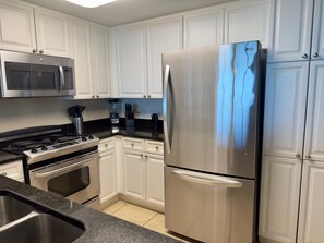 A kitchen with white cabinets, stainless steel appliances including a refrigerator, stove, and microwave, and a granite countertop. - Sunny Waterscape ground-floor condo with pools, hot tubs, & stunning Gulf views (Fort Walton Beach)