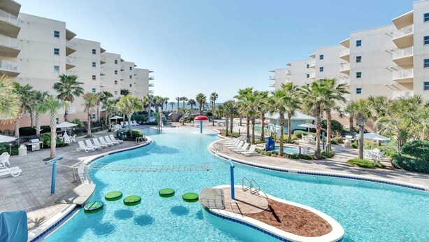 A swimming pool with lounge chairs and palm trees, surrounded by multi-story buildings. - Sunny Waterscape ground-floor condo with pools, hot tubs, & stunning Gulf views (Fort Walton Beach)