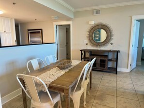 A dining area with a wooden table, white chairs, a lace table runner, and a decorative mirror on the wall. - Sunny Waterscape ground-floor condo with pools, hot tubs, & stunning Gulf views (Fort Walton Beach)