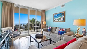 En rummelig stue med balkon, sofaarrangement, en fletstol og et glasbord.