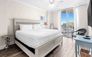 Ein Schlafzimmer mit Bett, kleinem Tisch, Stuhl, Deckenventilator und Blick auf die Stadt durch große Fenster.