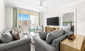 Ein modernes Wohnzimmer mit einer Sofagarnitur, einem Flachbildfernseher und einem Balkon mit Blick auf ein Hotel und Gebäude.