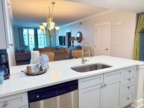 A kitchen with a dishwasher, a sink, and a dining area with a sofa and a television. - Spacious, Beachy Condo On Okaloosa Island w Playground and Two Hot Tubs Access (Fort Walton Beach)
