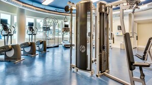 Uma academia com diversos equipamentos de exercícios, janelas amplas e teto azul.