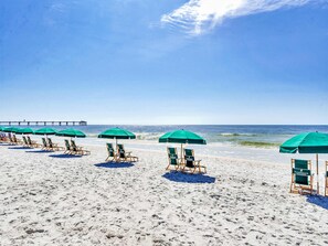 A beach with rows of green umbrellas and wooden lounge chairs. - Spacious, Beach-Chic Condo At Waterscape Steps To Beach Lazy River (Fort Walton Beach)