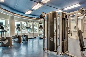 A modern gym with various exercise equipment, large windows, and a blue ceiling. - Tropical Condo On Okaloosa Island 490 Feet Of Private Beach (Fort Walton Beach)