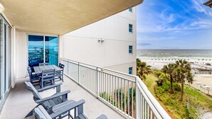 Varanda com mesa e cadeiras, vista para uma praia e um edifício com fachada branca.