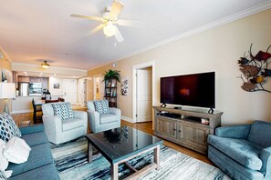 A spacious living room with a large flat-screen TV, two grey sofas, a coffee table, and a ceiling fan. - 4th Floor Condo At Waterscape Children's Playground, 2 Hot Tubs (Fort Walton Beach)