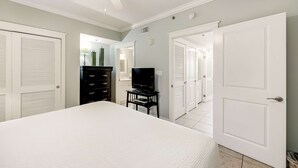Een slaapkamer met een bed, een televisie op een dressoir, een kast en witte deuren die naar andere kamers leiden.