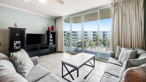 Een moderne woonkamer met een flatscreen-tv, een plafondventilator en een balkon met uitzicht op gebouwen.