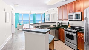 Una cucina moderna con vista sull'oceano, una zona pranzo e un balcone con tende blu.