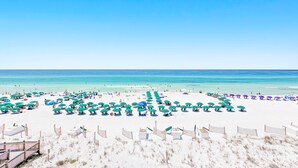 Una spiaggia con file di ombrelloni e lettini, una recinzione in legno e una passerella che conduce alla spiaggia.